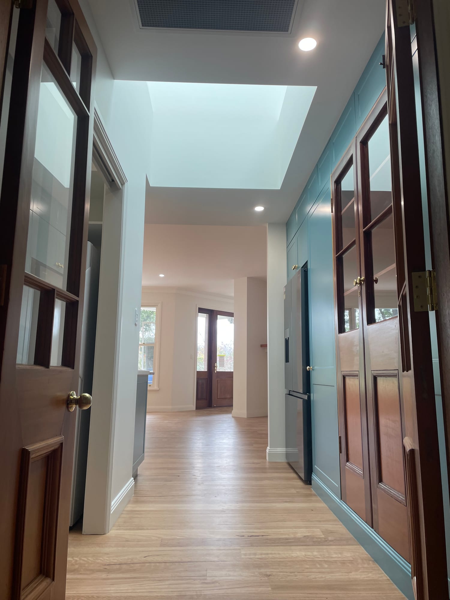 Skylit hallway with teal joinery and timber-framed glass doors